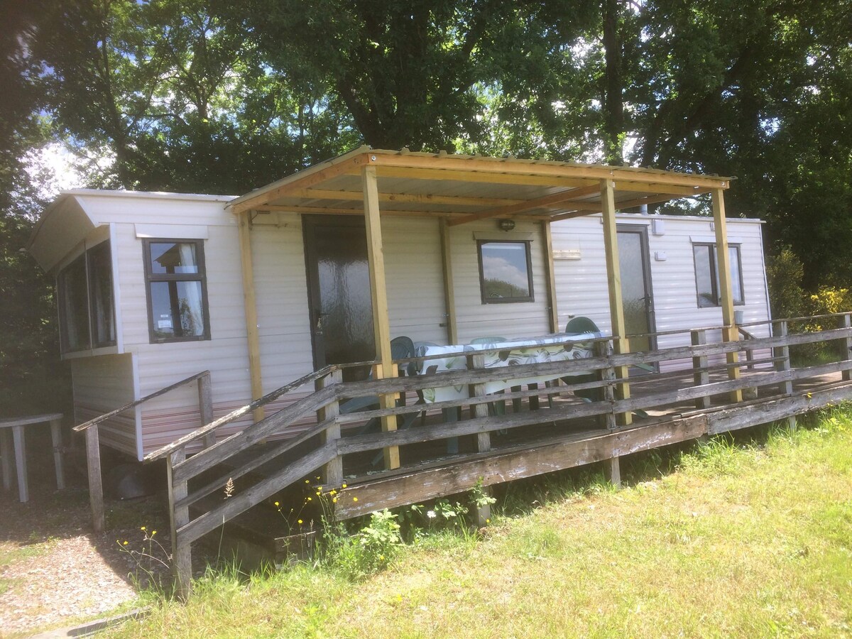 Un mobil-home avec terrasse à côté d'étang.