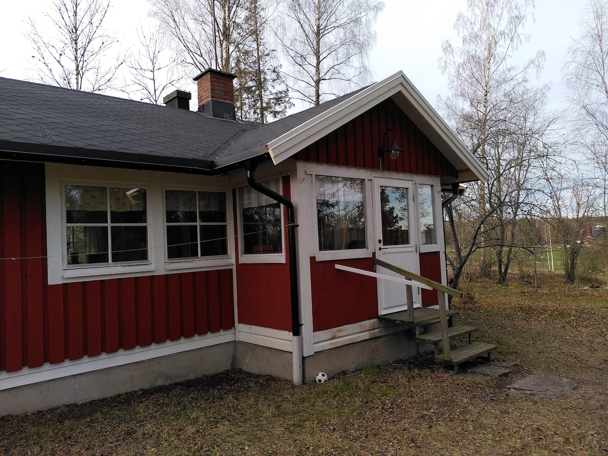 Mysig röd stuga med vita knutar i vacker natur.